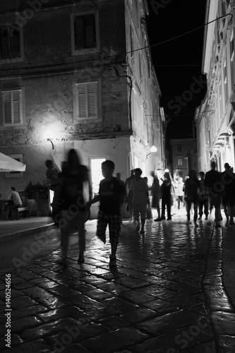 Groups of tourists on the night street of an ancient city on the Adriatic coast. Croatia.
