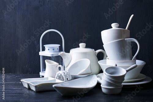 Set of new white dishes with teapot, tea cups, and plates on a black wooden table