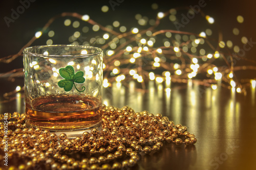 Irish Whiskey St Patricks Clover. Irish whiskey in a glass with a clover symbol, on a pub table with gold beads and bar lights.