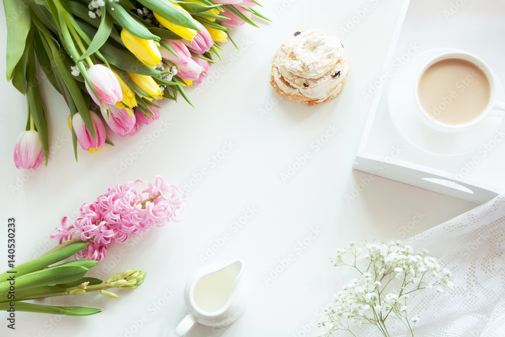 Morning breakfast in spring with a cup of black coffee with milk and pastries in the pastel colors, a bouquet of fresh yellow and pink tulips on a white background. Top view.