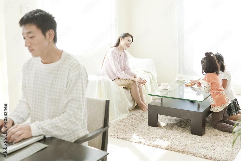 Family of Four in Living Room, Father Using Laptop Family of Four in Living Room, Father Using Laptop
