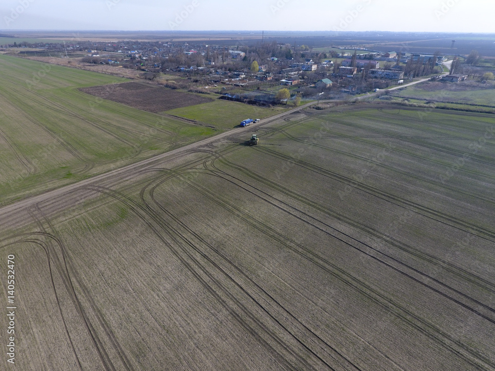 Fototapeta premium Tractor with hinged system of spraying pesticides. Fertilizing with a tractor, in the form of an aerosol, on the field of winter wheat.