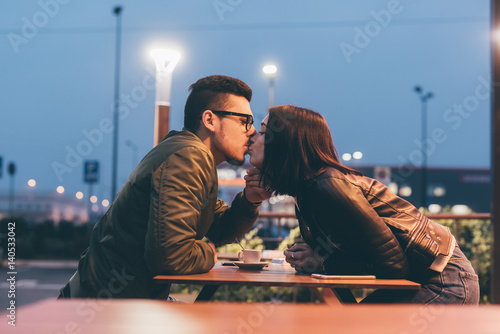 Young beautiful couple sitting outdoor in the night kissing - kiss, love, relationship concept
