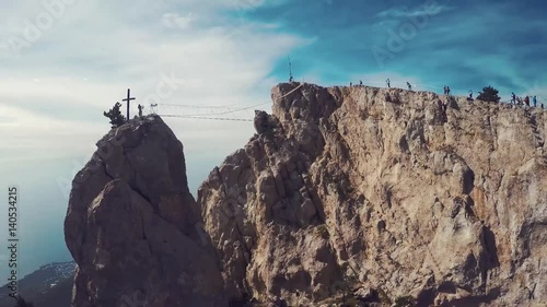 Apic aerial shot of man walking suspension bridge to Cross in Crimea. High rocks Ai-Petri of Crimean mountains. Black sea coast city and blue sky with clouds. photo