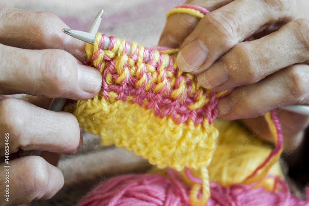 Women's hands hold knitting needles and a yellow thread to tie a scarf from them Women's hands hold knitting needles and a yellow thread to tie a scarf from them