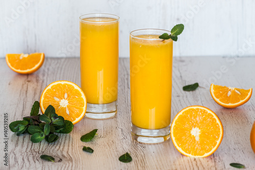 orange juice with mint in glasses at light wooden background