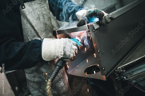 Metallurgy industry. Factory for production of heavy pellet stoves and boilers. Manual worker welder on his job. Extremely dark conditions and visible noise. Focus on foreground.