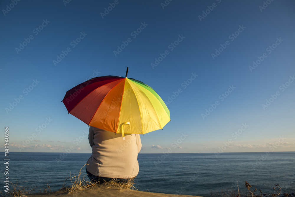 Woman watching the sea with the umbrella in the rainbow color