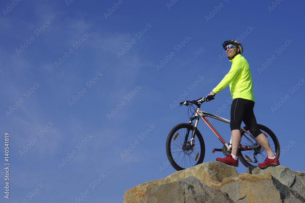 Smile man, in light-green jacket and red sneakers, near mountain bike with sky background