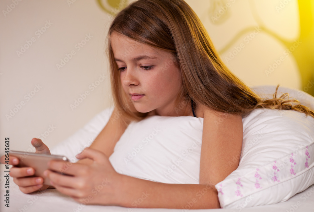 Young girl using smartphone lying in bed, shallow depth Young girl using smartphone lying in bed, shallow depth