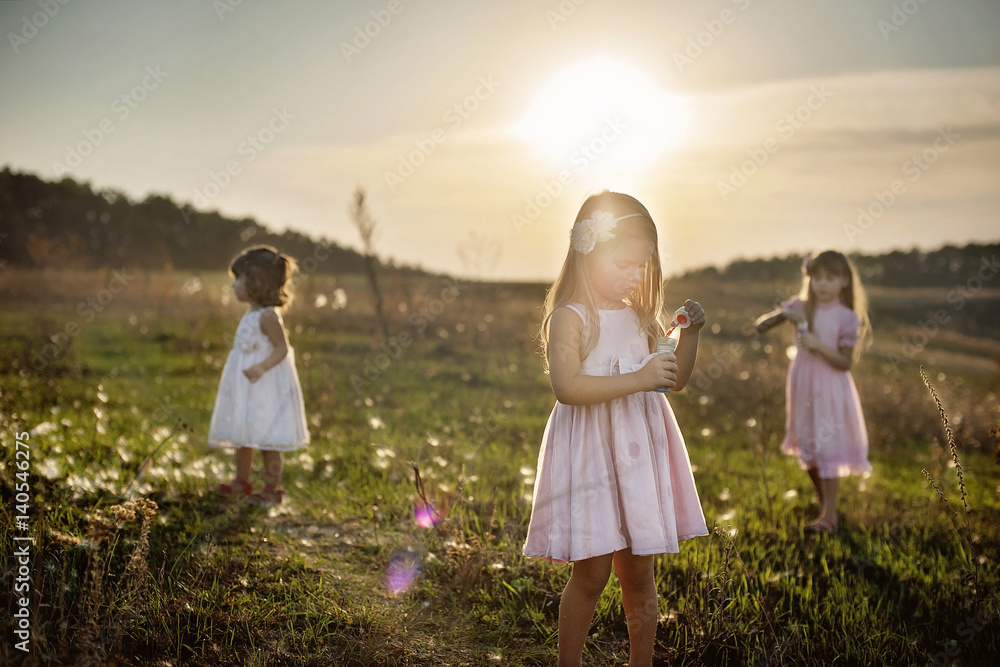 Three little girls at the green field in sunset time, with bubbles Three little girls at the green field in sunset time, with bubbles