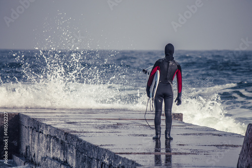 Surfer goes into water wearing a wetsuit in winter. Cold surfing. Wave splash. waterproof suit