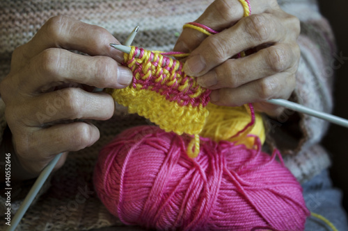 Women's hands hold knitting needles and a yellow thread to tie a scarf from them