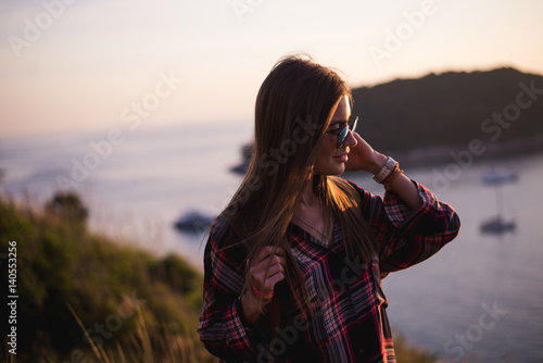 Young stylish hipster girl enjoy sunset on viewpoint. Travel woman with backpack