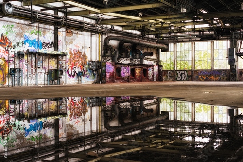 Verlassene Fabrikhalle mit riesiger Pfütze und Graffiti