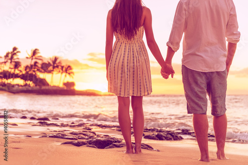 Couple from behind relaxing watching sunset on hawaiian beach together holding hands