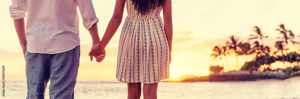 Couple watching sunset on hawaiian beach together, relaxing holding hands panorama banner. Man, woman in love concept. Couple watching sunset on hawaiian beach together, relaxing holding hands panorama banner. Man, woman in love concept.