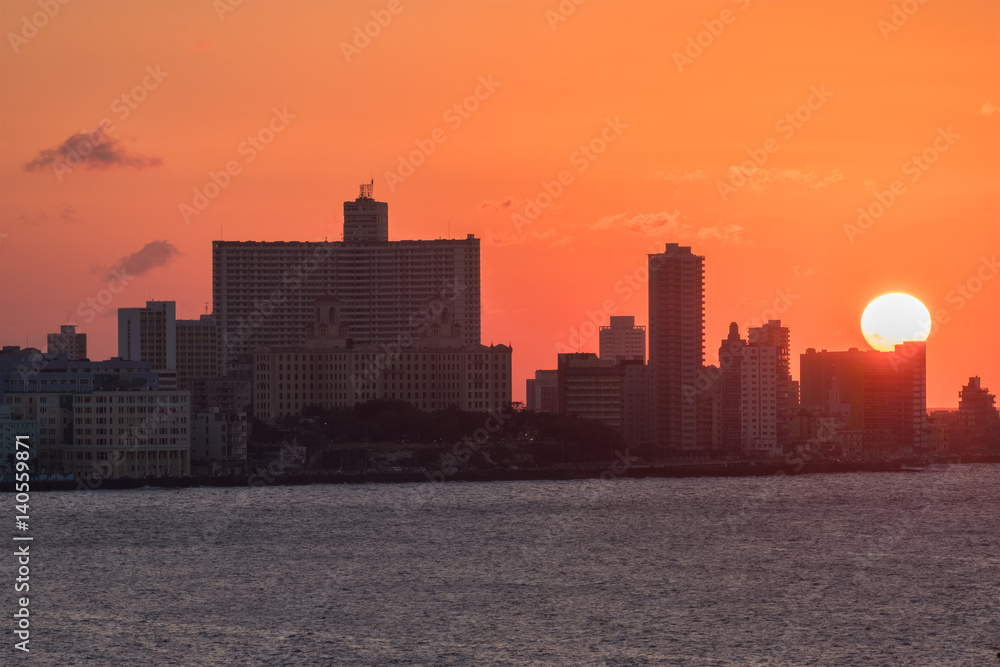 The city of Havana at sunset with the sun setting over seaside tall buildings