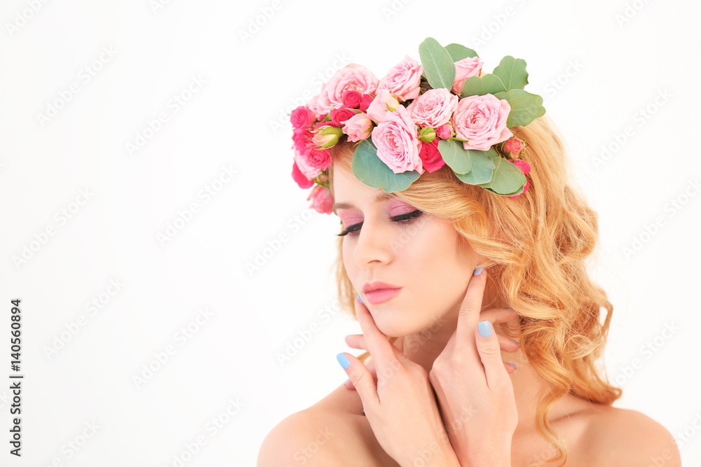 Beautiful young woman with flowers in hair on white background