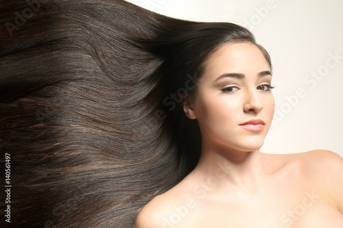 Beautiful young woman with long straight hair on light background