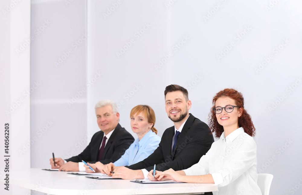 Group of four business people in elegant suits sitting at working desk in light auditorium Group of four business people in elegant suits sitting at working desk in light auditorium
