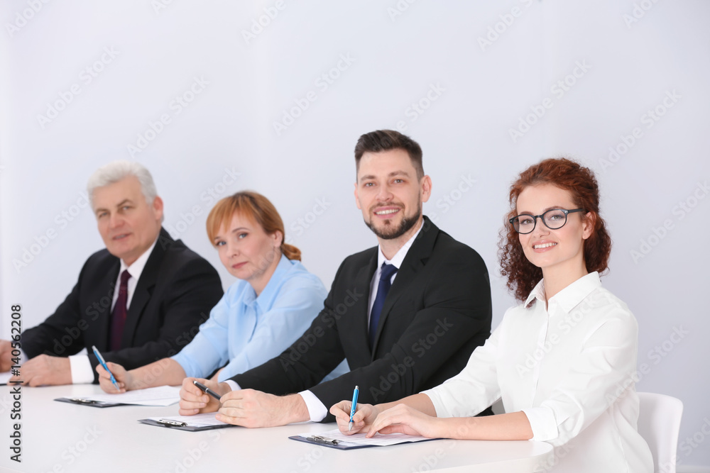 Group of four business people in elegant suits sitting at working desk in light auditorium Group of four business people in elegant suits sitting at working desk in light auditorium