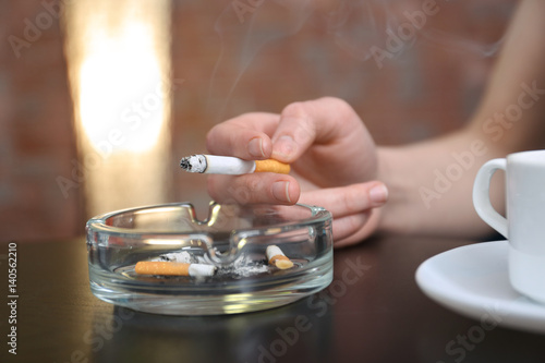 Smoking woman's hand holding cigarette sitting at table