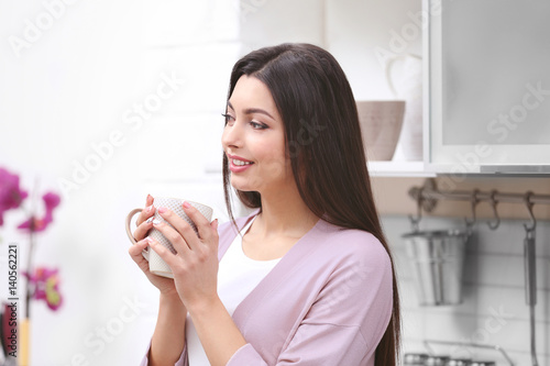 Fototapeta Naklejka Na Ścianę i Meble -  Beautiful young woman drinking coffee in kitchen