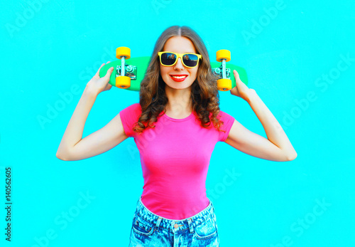 Fashion pretty young woman holds skateboard over colorful blue background