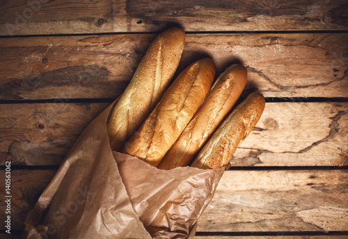 Four baguette bread loaves in paper bag on wooden background