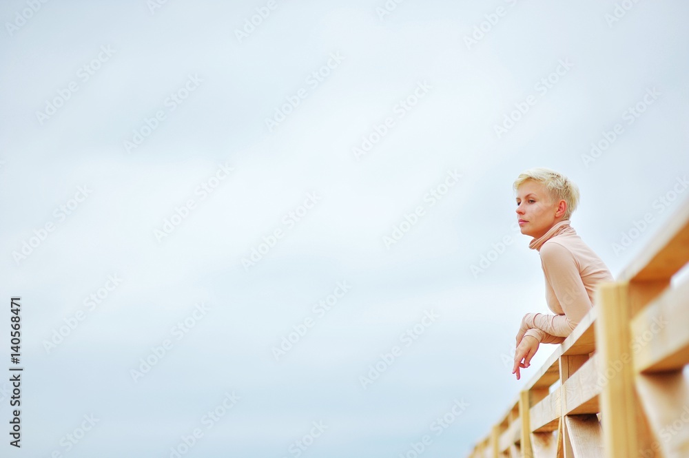 Portrait of a young pretty girl blonde enjoying fresh air, standing on the wooden deck against clear sky Portrait of a young pretty girl blonde enjoying fresh air, standing on the wooden deck against clear sky