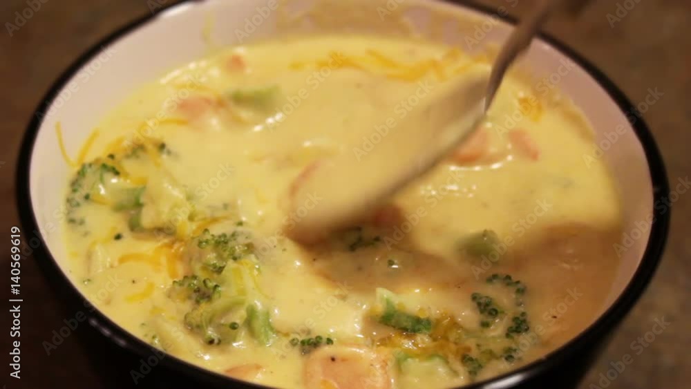 Spoon stirs broccoli cheddar soup Spoon stirs broccoli cheddar soup