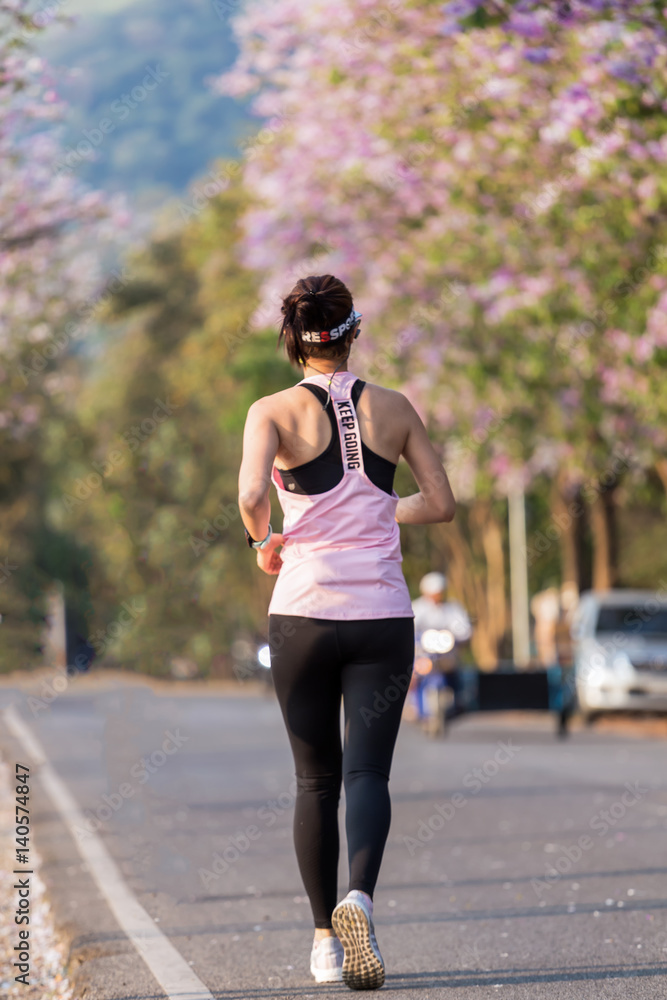 Healthy young brunette woman out jogging alone on a tarred road surrounded with a forest of trees Healthy young brunette woman out jogging alone on a tarred road surrounded with a forest of trees