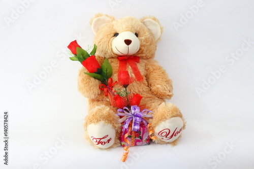Brown teddy bear with a red rose and a gift box on a white background.