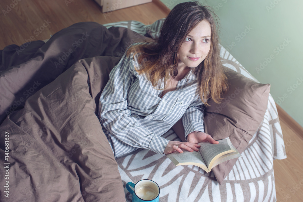 Obraz premium Cute girl reading a book while lying in bed