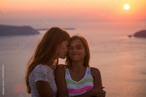 Mother and daughter at sunset. Sunset on the island of Santorini.  Girl tourist on a background of the sea and the setting sun. Mother and daughter travel  Mother s love  Girl teenager and her mom.  