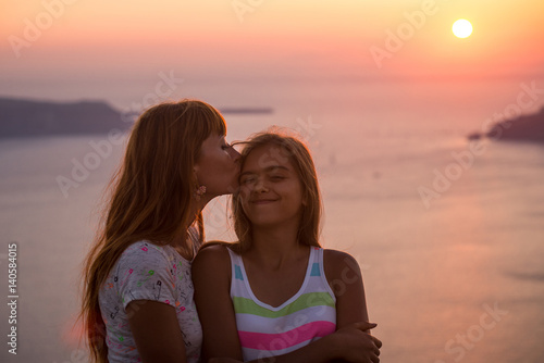 Mother and daughter at sunset. Sunset on the island of Santorini. Girl tourist on a background of the sea and the setting sun. Mother and daughter travel, Mother's love, Girl teenager and her mom. 
