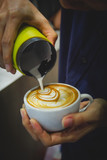 Barista pouring milk from pitcher to a cup of coffee making latte art