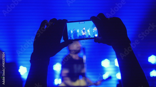 Fans hands recording video with smart phones at rock concert in beautiful blue colors on the background