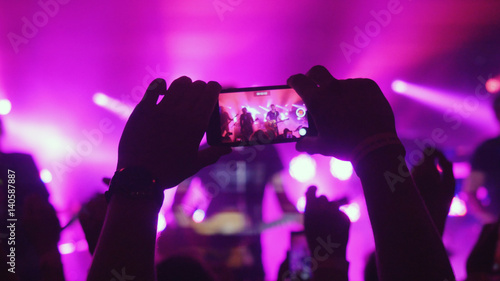 Fans womans hands recording video with smart phones at rock concert on pink colors