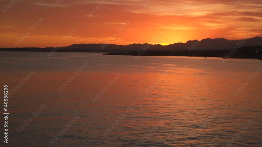 The light of the sun at sunset reflects in the sea. On the horizon there are mountains The light of the sun at sunset reflects in the sea. On the horizon there are mountains