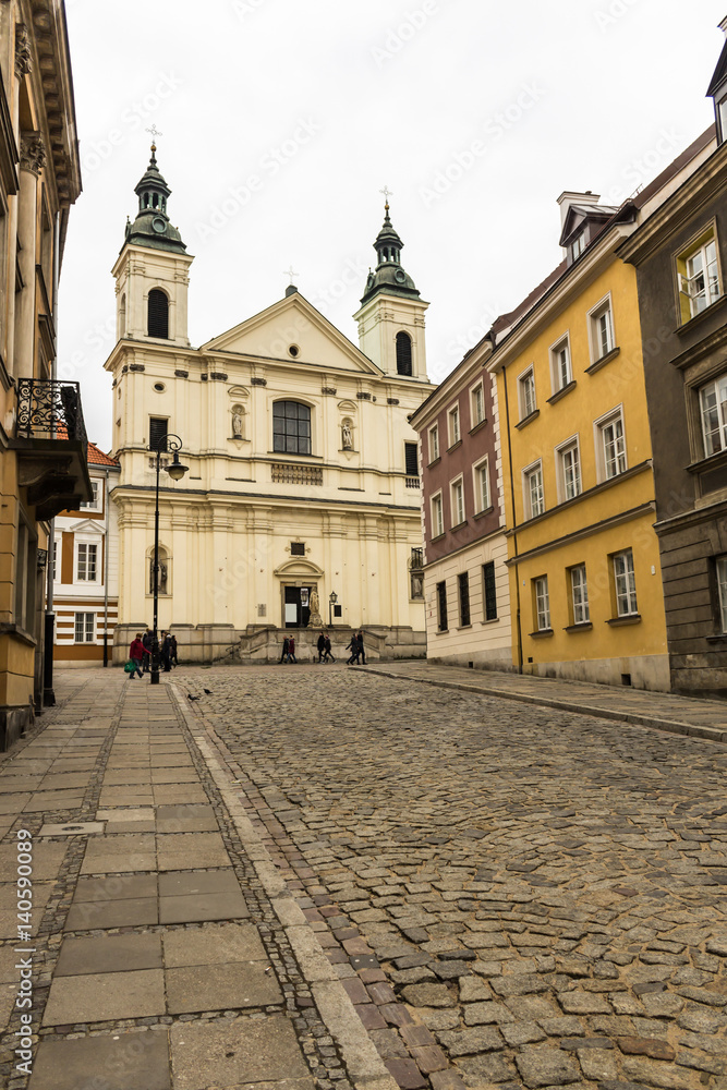 The area of the Old Town in Warsaw, Poland . An old street with nineteenth-century houses, a street lamp and a baroque church.
