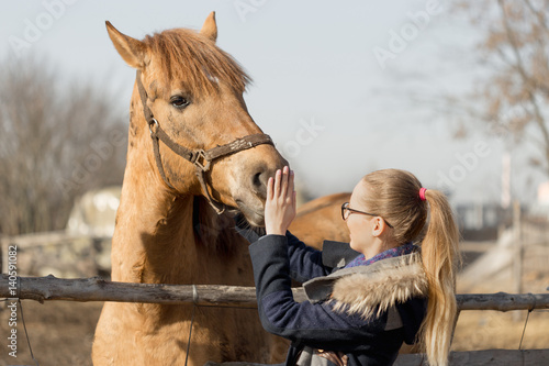 Girl stroking a thoroughbred horse in the pen for paddock