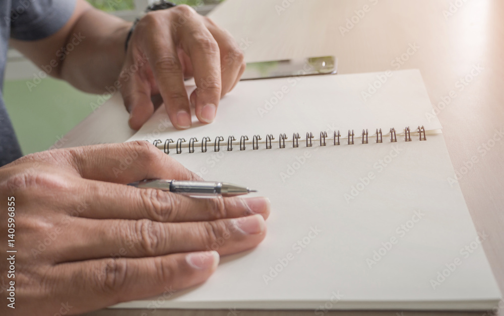 Man hand with pen writing on notebook and smart-phone on the desk.