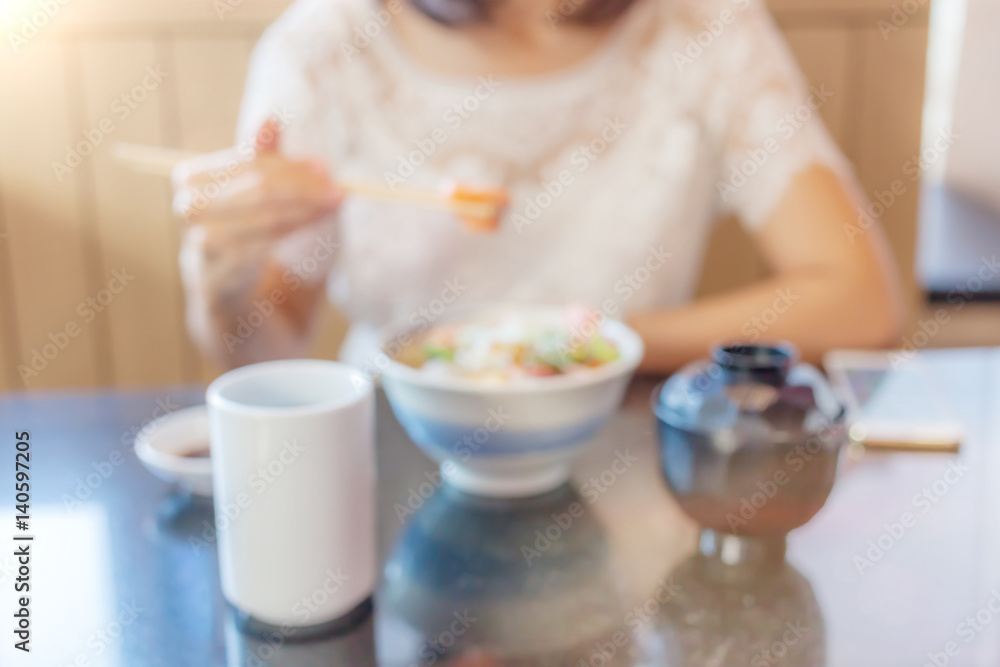 Blurred photo of woman is holding the chopsticks and enjoying the Japanese food on her front. Blurred photo of woman is holding the chopsticks and enjoying the Japanese food on her front.