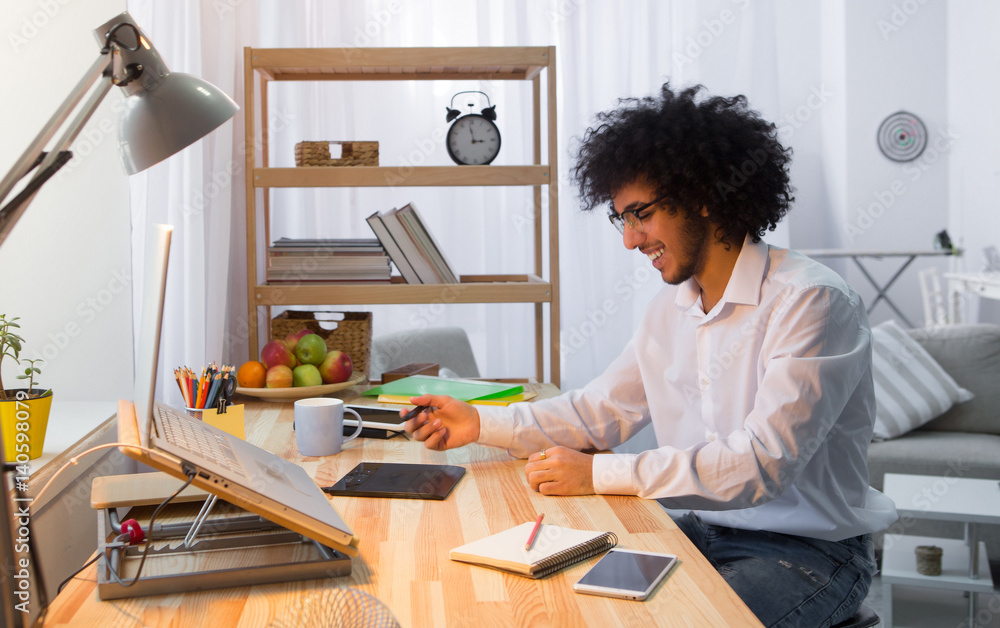 Handsome hipster freelance man using editing board for editing photos or videos while working at table and using laptop computer at home alone. Handsome hipster freelance man using editing board for editing photos or videos while working at table and using laptop computer at home alone.