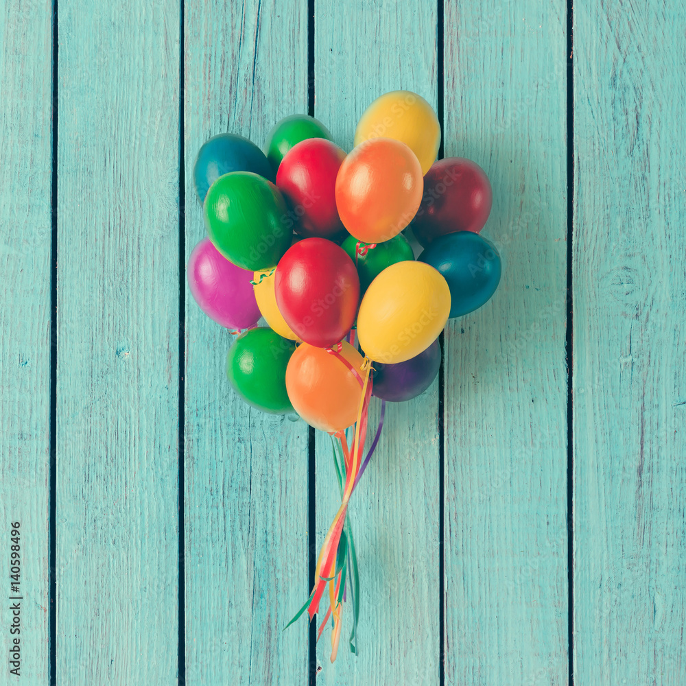 Fototapeta premium Colorful bunch of Easter egg balloons on blue wooden background. Minimal creative concept. Flat lay.