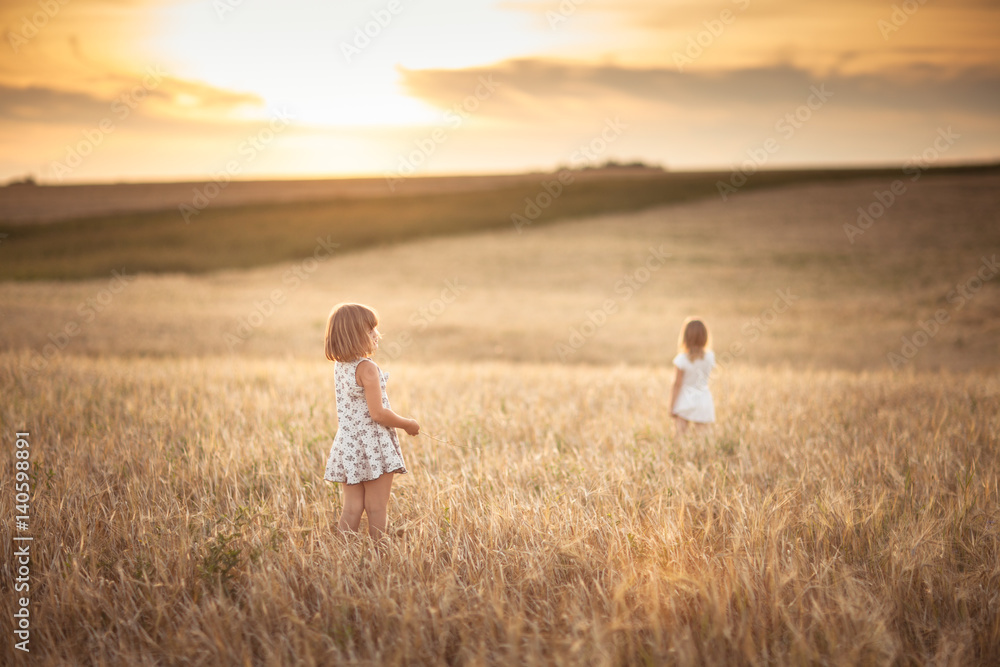 Sisters girls walk in the field with rye sunset