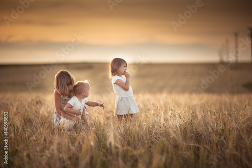 Three girls sisters walk in field with rye sunset