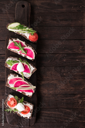 Sandwiches with cream cheese and fresh cucumber, radish,tomatoes,arugula and mozzarella. Fresh healthy appetizer snack with crispbread.